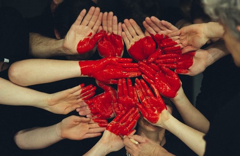 Many hands painted together to form one red heart